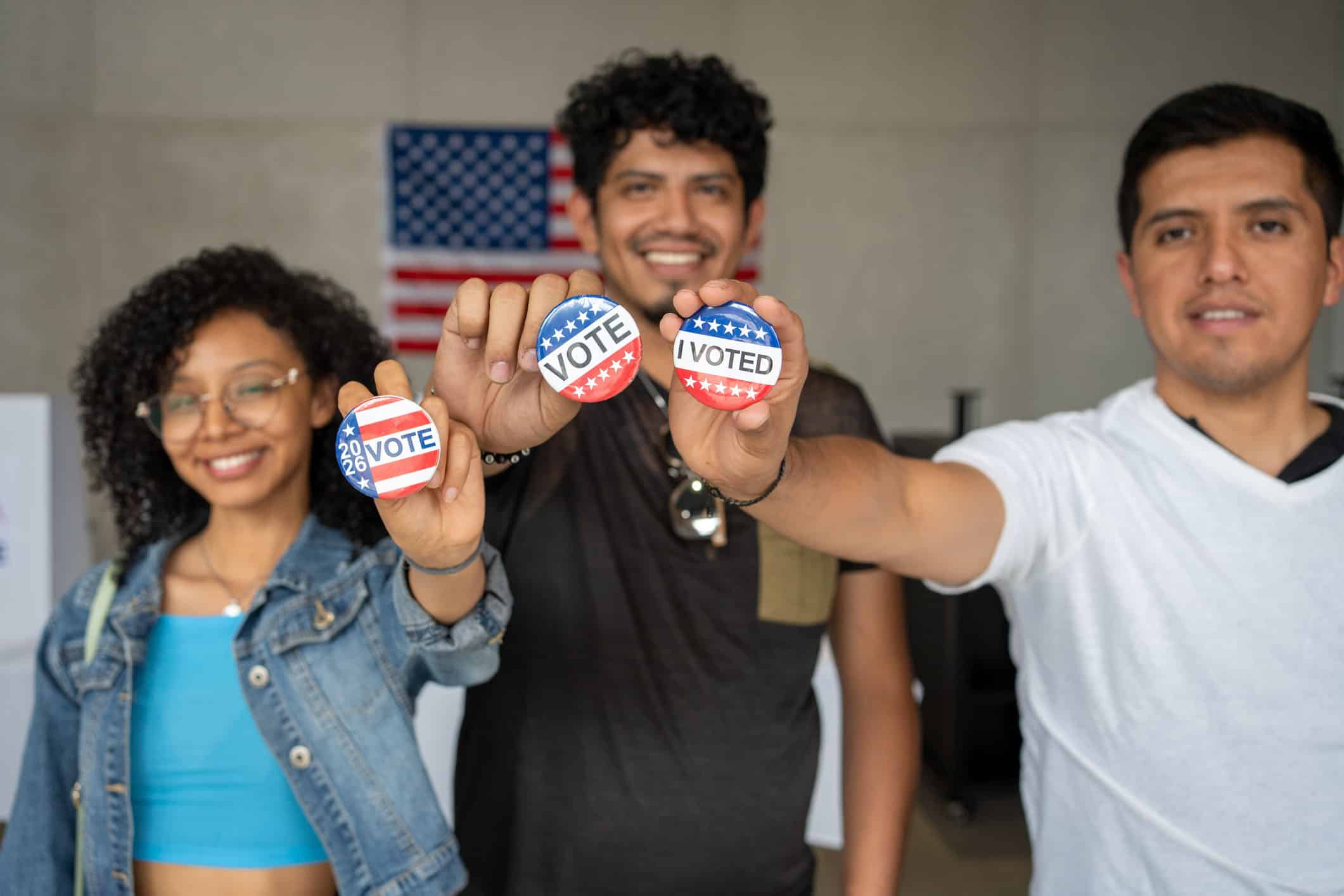 Three diverse teenagers holding 'I Voted' pins and smiling at the camera